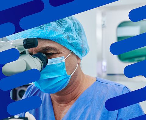 Surgeon wearing a mask and surgical cap looking through an ophthalmic microscope in an operating room.