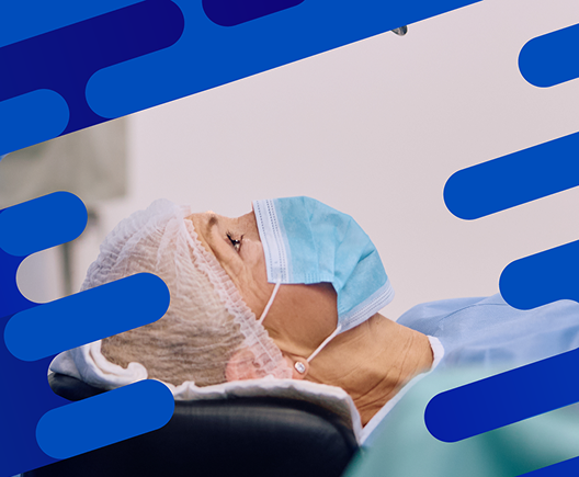Patient wearing a surgical cap and mask lying beneath a Centurion Vision System monitor during an ophthalmic procedure.