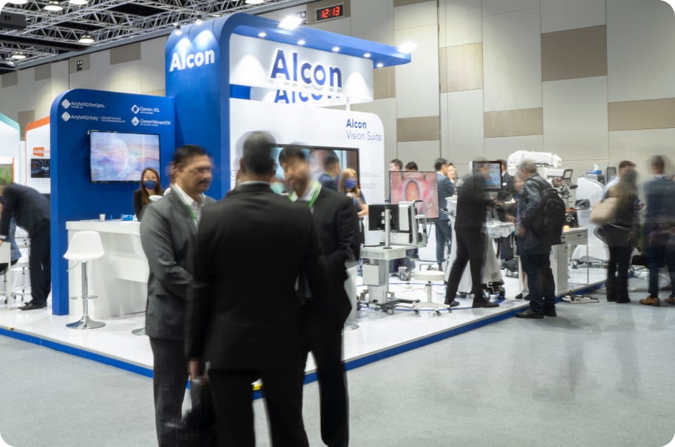 Alcon exhibition booth at a medical conference with attendees exploring ophthalmic equipment and engaging in discussions.