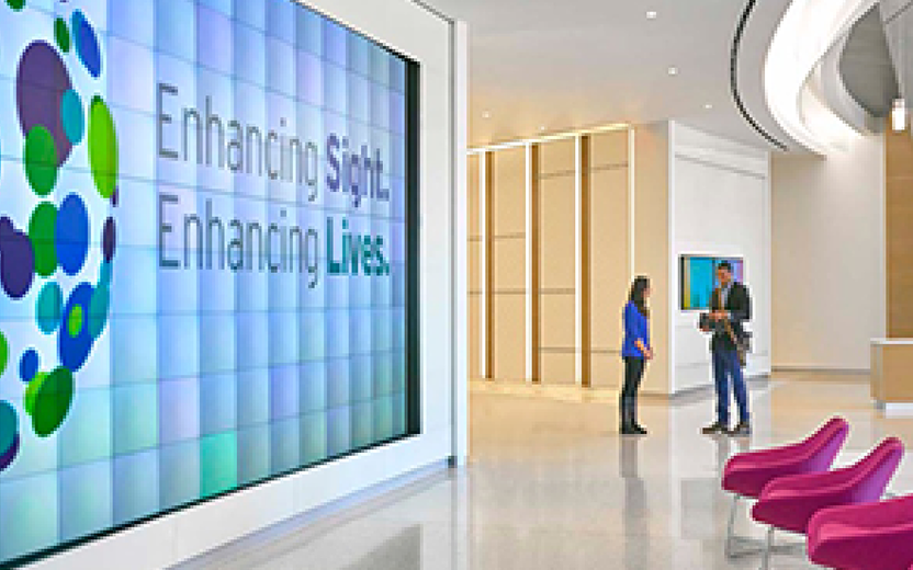 An image of two people standing in a convention center with a large screen.