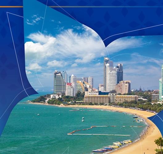 A tropical coastal city with modern high-rise buildings along a curved sandy beach, turquoise sea waters, and small boats near the shore, displayed within a stylized blue graphic frame