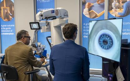 People viewing a surgical microscope demonstration with a large monitor displaying a close-up image of an eye.